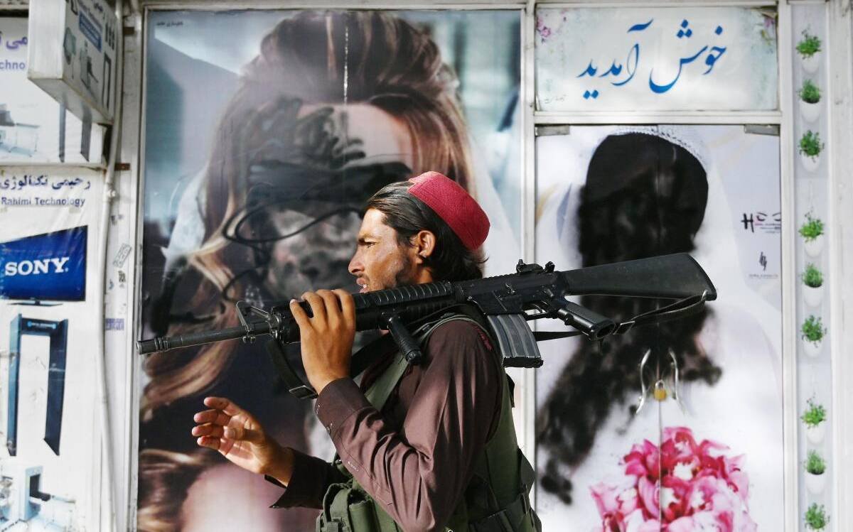 A Taliban fighter walks past a beauty saloon with images of women defaced using a spray paint in Shar-e-Naw in Kabul on August 18, 2021.   | Photo Credit: AFP